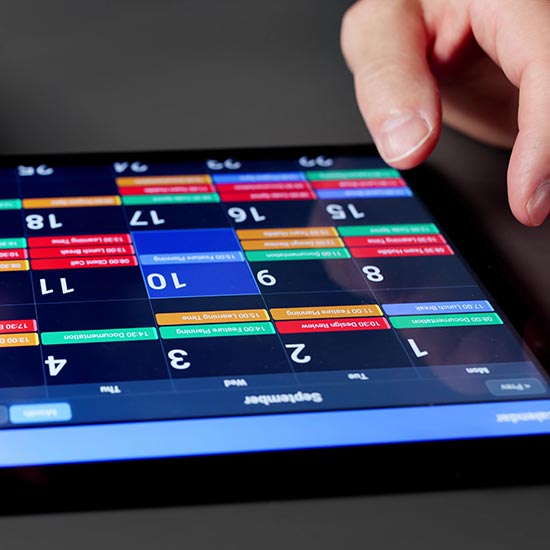 2026 Education Calendar; A hand interacts with a digital calendar on a tablet, displaying a colorful, dense schedule. The layout suggests a busy and organized day.