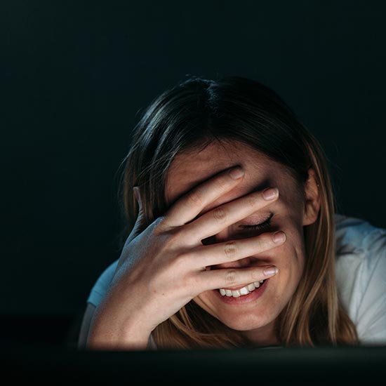Tech Talk: Confessions of a Cybersecurity Pro Who Failed a Phishing Test; A woman smiles with her hand covering her face, conveying amusement. The lighting is dim, suggesting an intimate, cozy atmosphere.